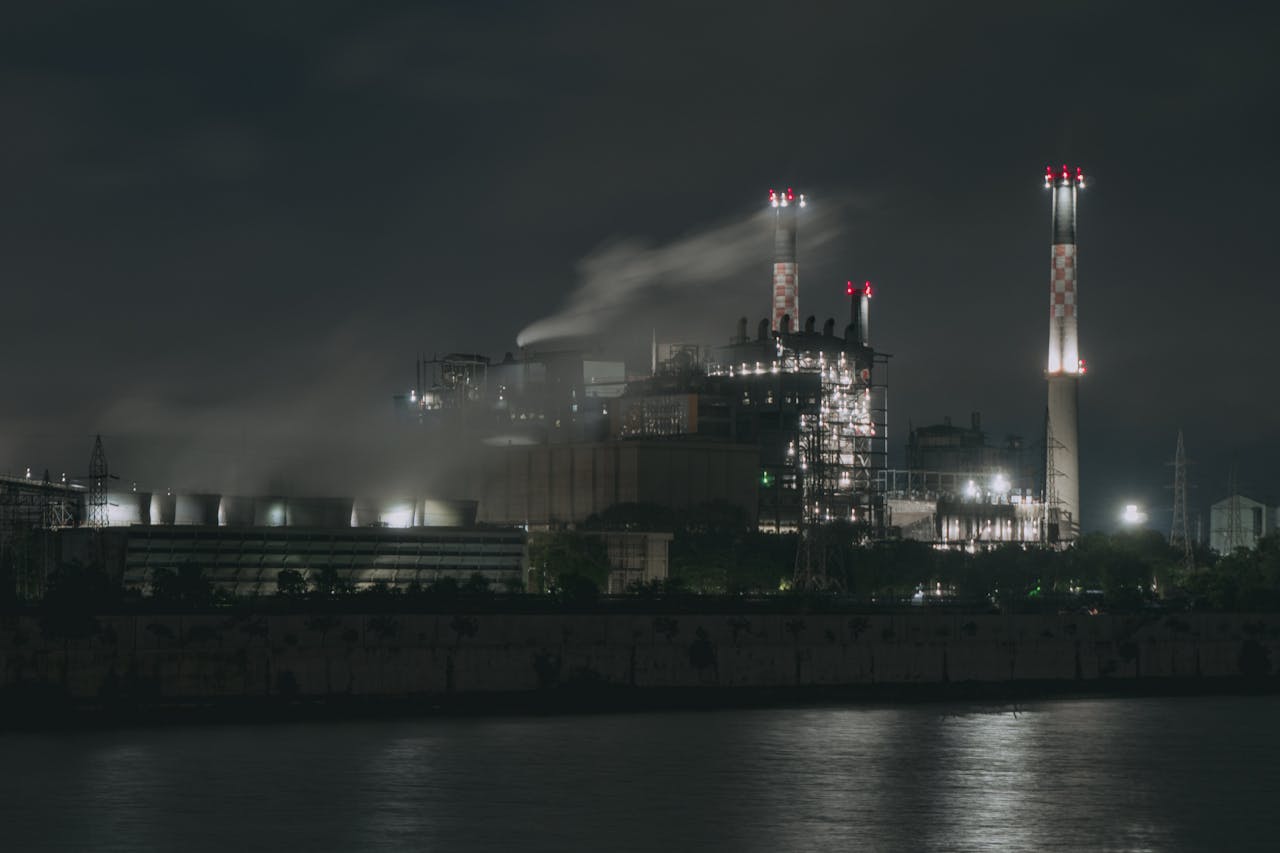Night view of a large industrial factory with chimneys emitting smoke by the river in Ahmedabad, India.