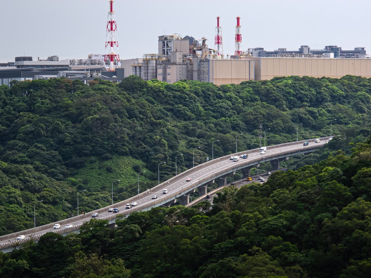 Elevated highway weaving through green forest and industrial area in Taiwan, showcasing nature and industry.
